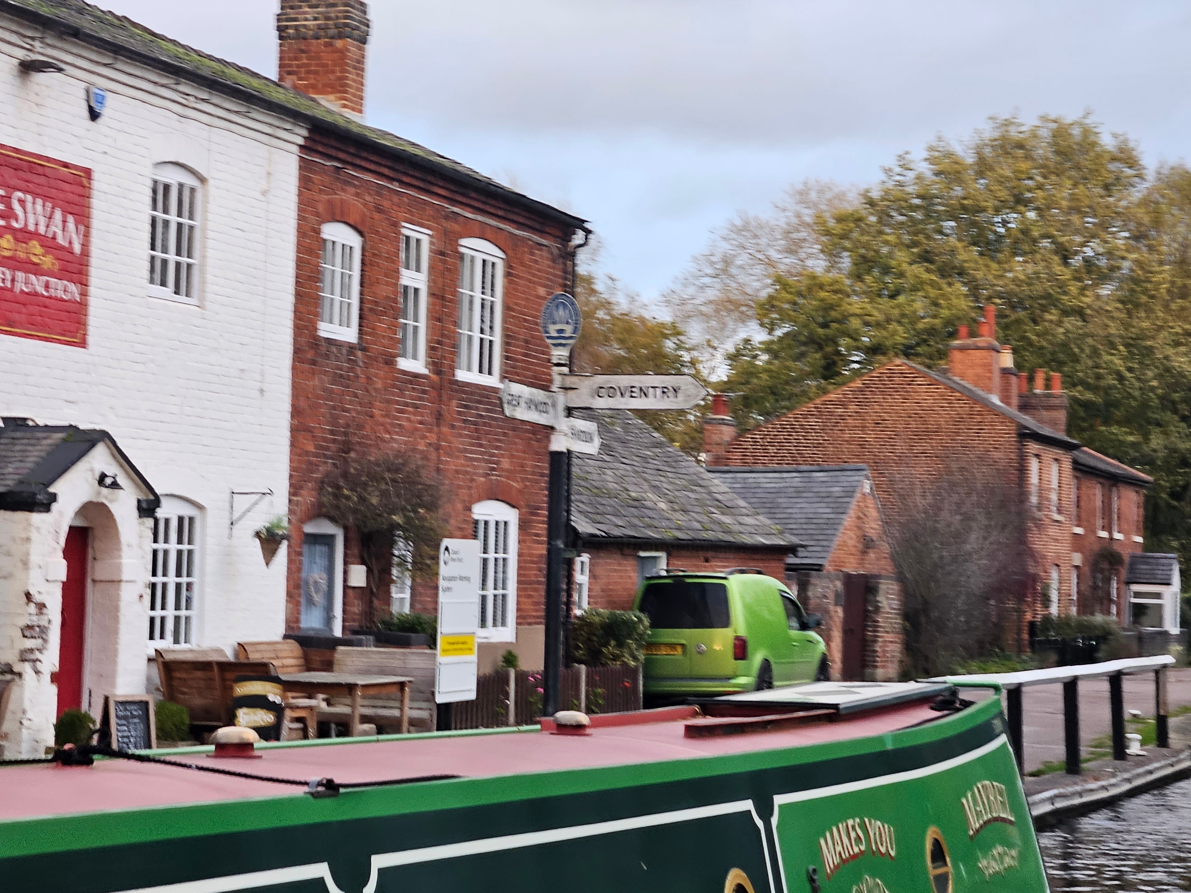 A canalside pub, brick built and part painted white, with a signpost on the towpath outside which points to the Coventry canal junction