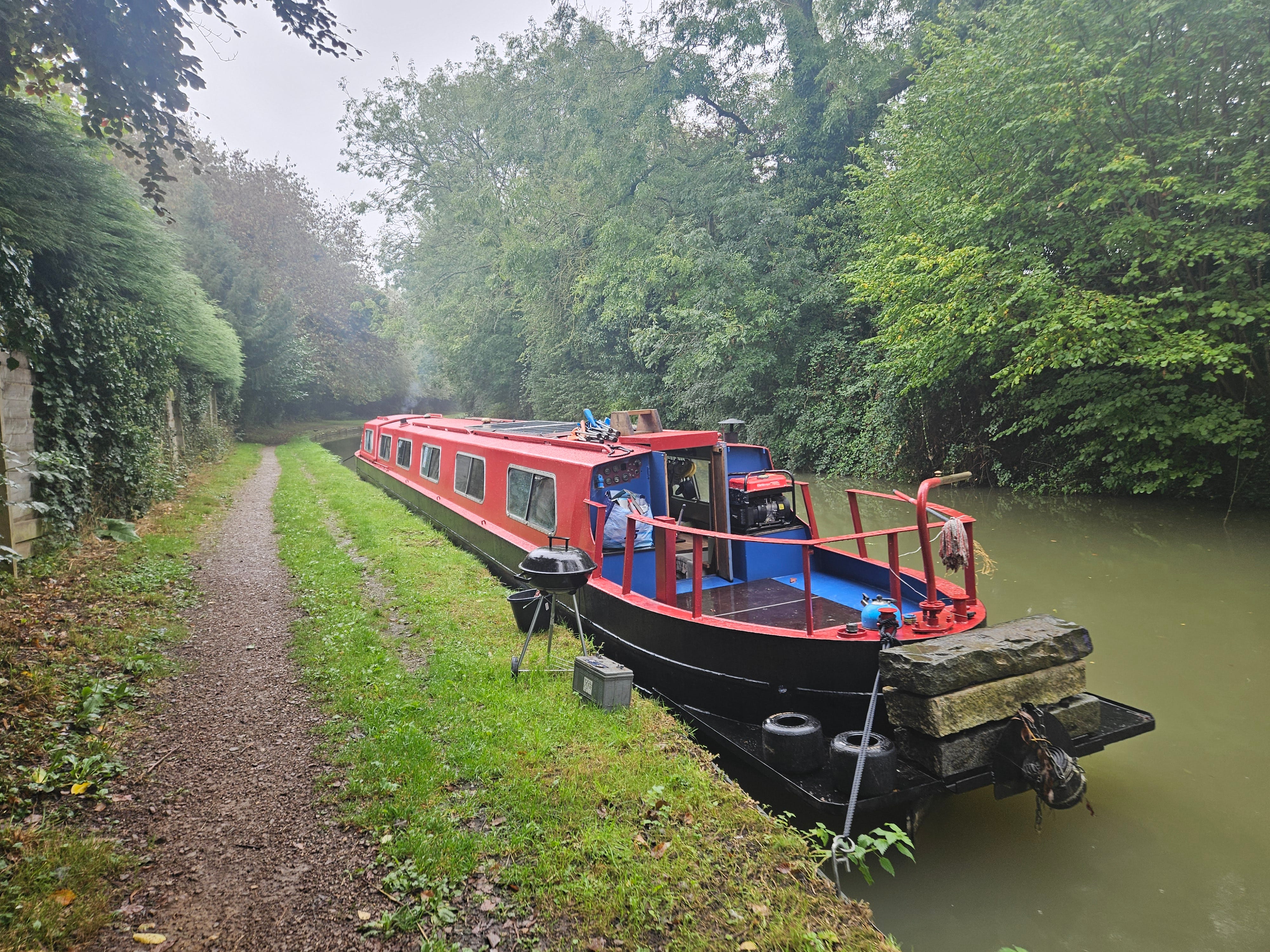 A red narrowboat photographed in leafy surroundings