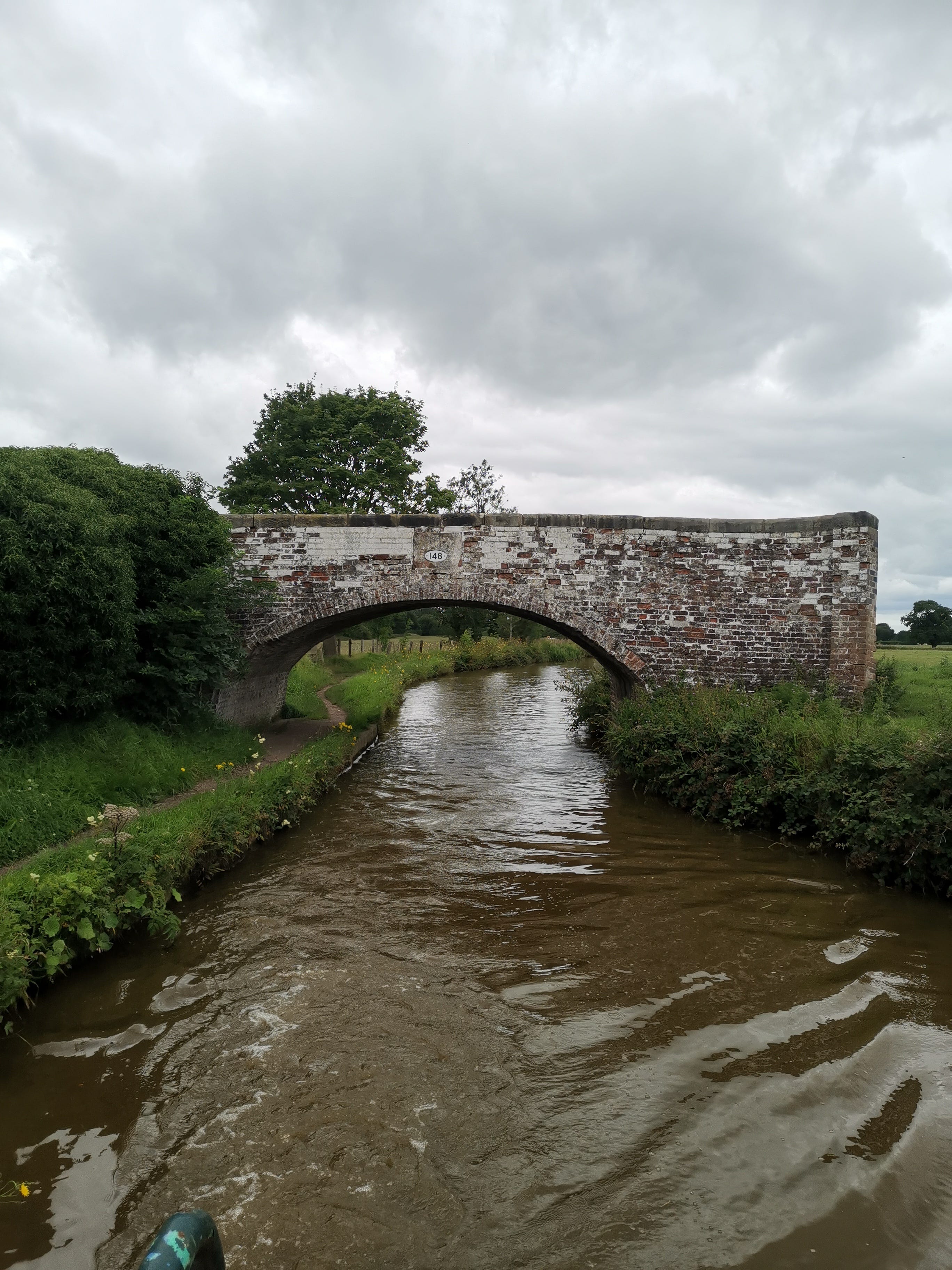 A brick build arch bridge over a canal with path to the left. The brick is painted white, now faded